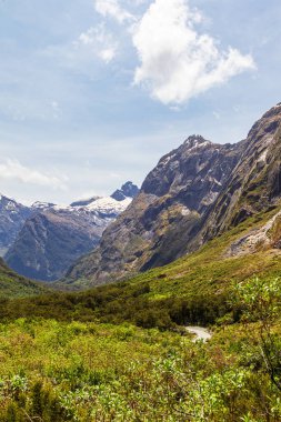 Bulutlardaki sarp kayalıklar ve Fiordland yolunda yeşil bir vadi. Yeni Zelanda