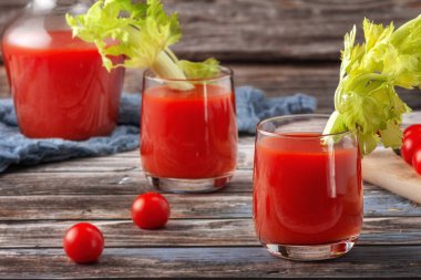 Bir ağacın arka planında, ahşap bir masada iki bardak domates suyu, taze bir içecek