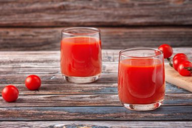 Bir ağacın arka planında, ahşap bir masada iki bardak domates suyu, taze bir içecek