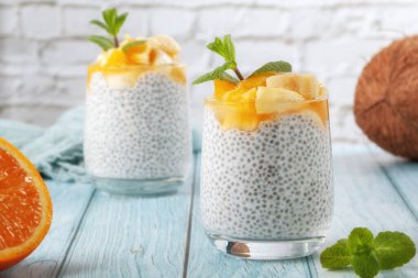 Mavi ahşap bir masada, çiğ chia tohumlu iki cam bardakta muzlu chia pudingi.