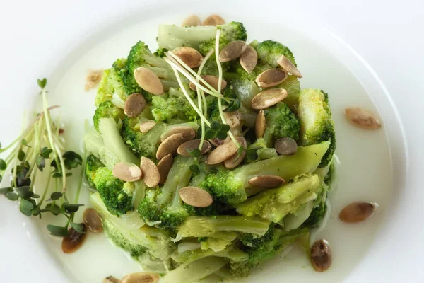 Gekookte broccoli met pompoenpitten op een wit bord op tafel — Stockfoto
