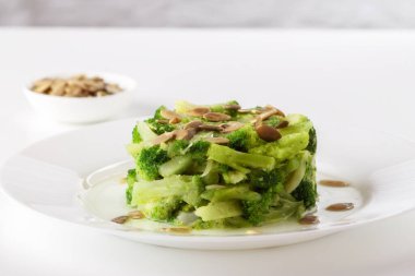 Masanın üzerinde, kaynamış brokoli ve beyaz bir tabakta kabak çekirdeği.