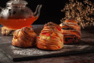 Masanın üzerinde kraffinler, şekerli meyveler ve haşhaş tohumları var, üzerine toz şeker serpiştirilmiş..