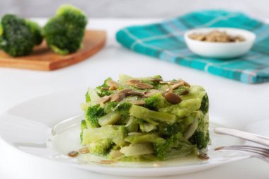 Masanın üzerinde, kaynamış brokoli ve beyaz bir tabakta kabak çekirdeği.