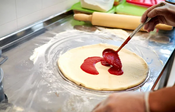 Preparing pizza at restaurant. The chef cooks Italian pizza, topping with sauce.