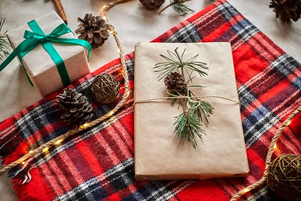 Christmas gifts on the background of a red woolen checkered plaid with garlands of cones and fir branches. gift wrapping for a book or laptop in craft paper