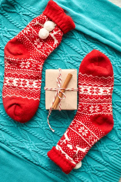 Christmas composition, red socks with a gift on a blue knitted sweater with a garland and cones