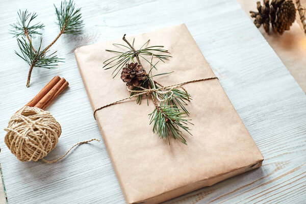 подарочная упаковка для книги или ноутбука в бумагу, связанную веревкой и украшенную еловой веткой с конусом
