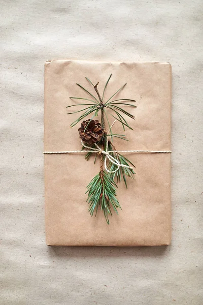 gift wrapping for a book or laptop in craft paper tied with twine rope and decorated with a fir branch with a cone