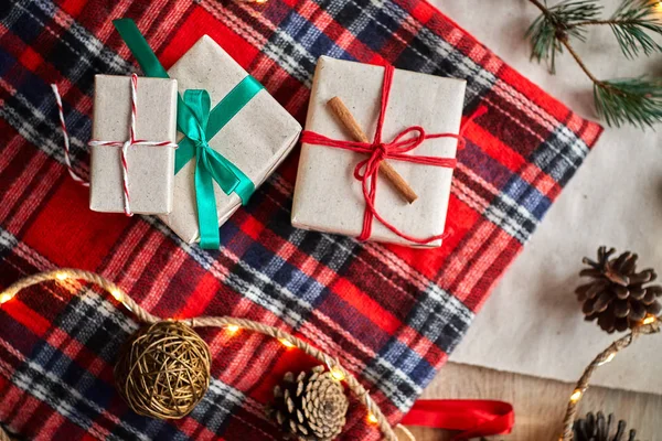 Christmas gifts on the background of a red woolen checkered plaid with garlands of cones and fir branches, a beautiful still life