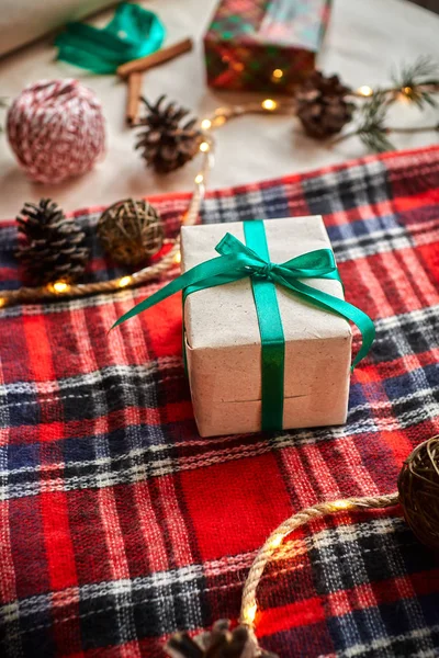 コーンとモミの枝のガーランドで演奏赤い毛織の小切手の背景にクリスマスの贈り物 — ストック写真