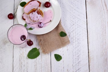 Kirazlı beyaz tabakta nefis krepler ve nane yapraklı açık ahşap zemin üzerinde cam bir fincanda yoğurt. Sağlıklı beslenme ve harika bir kahvaltı konsepti.