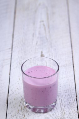 Hafif ahşap zemin üzerinde yabanmersinli yoğurt bulunan cam bardak. Güzel bir sabahta sağlıklı bir kahvaltı.