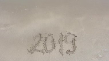 2019 'da kumsalda ıslak kumda yazılmış. Dalga yazıtlara yaklaşıyor, ama onu yıkamıyor. 2020 'ye yaklaşma konsepti. Tropik plajdaki yazıt..