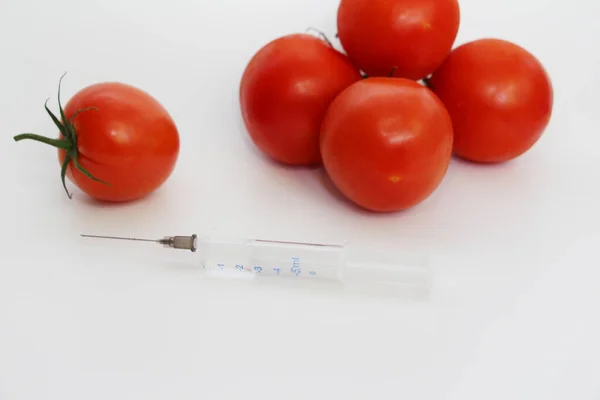 On a light background are red tomatoes and one syringe. — Stock Photo, Image