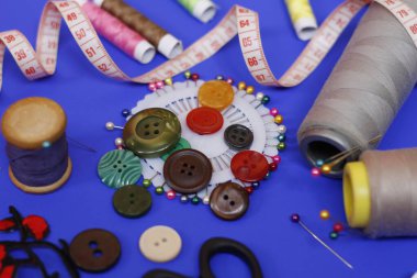 Mavi arkaplanda düğmeler ve iplikler dikiliyor.