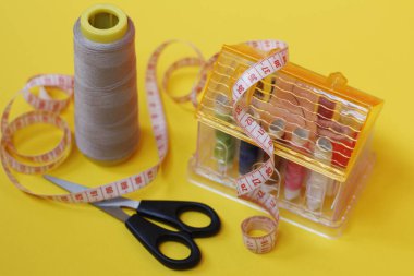 Sarı arka planda düğmeler ve iplikler dikiliyor.