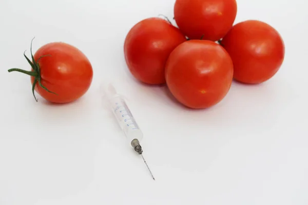 On a light background are red tomatoes and one syringe. — Stock Photo, Image