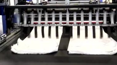 Video, plastik poşet üreten bir fabrikayı gösteriyor. Şaftlar dönüyor. Selofan şaftlar arasında hareket ediyor. Polietilen poşet üretimi için kullanılan bir makinenin parçaları.