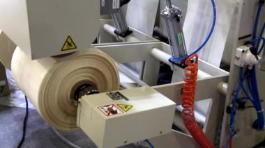 Video, plastik poşet üreten bir fabrikayı gösteriyor. Şaftlar dönüyor. Selofan şaftlar arasında hareket ediyor. Polietilen poşet üretimi için kullanılan bir makinenin parçaları.