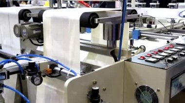 Video, plastik poşet üreten bir fabrikayı gösteriyor. Şaftlar dönüyor. Selofan şaftlar arasında hareket ediyor. Polietilen poşet üretimi için kullanılan bir makinenin parçaları.