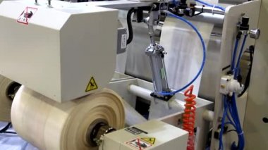Video, plastik poşet üreten bir fabrikayı gösteriyor. Şaftlar dönüyor. Selofan şaftlar arasında hareket ediyor. Polietilen poşet üretimi için kullanılan bir makinenin parçaları.