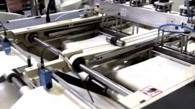 Video, plastik poşet üreten bir fabrikayı gösteriyor. Şaftlar dönüyor. Selofan şaftlar arasında hareket ediyor. Polietilen poşet üretimi için kullanılan bir makinenin parçaları.