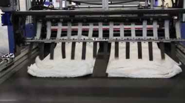 Video, plastik poşet üreten bir fabrikayı gösteriyor. Şaftlar dönüyor. Selofan şaftlar arasında hareket ediyor. Polietilen poşet üretimi için kullanılan bir makinenin parçaları.