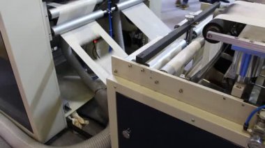 Video, plastik poşet üreten bir fabrikayı gösteriyor. Şaftlar dönüyor. Selofan şaftlar arasında hareket ediyor. Polietilen poşet üretimi için kullanılan bir makinenin parçaları.