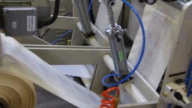 Video, plastik poşet üreten bir fabrikayı gösteriyor. Şaftlar dönüyor. Selofan şaftlar arasında hareket ediyor. Polietilen poşet üretimi için kullanılan bir makinenin parçaları.