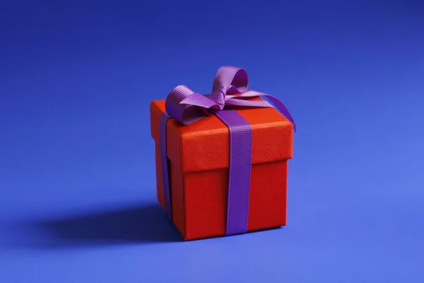 Όμορφο κόκκινο κουτί δώρου με ένα μωβ τόξο σε μπλε φόντο. — Φωτογραφία Αρχείου