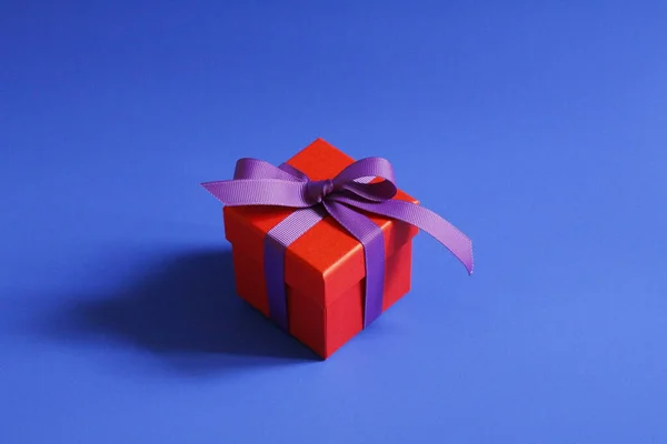 Όμορφο κόκκινο κουτί δώρου με ένα μωβ τόξο σε μπλε φόντο. — Φωτογραφία Αρχείου