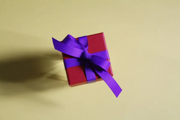 Bella scatola regalo rossa con un fiocco viola su uno sfondo giallo . — Foto Stock