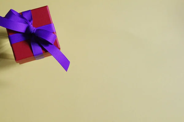 Όμορφο κόκκινο κουτί δώρου με ένα μωβ τόξο σε κίτρινο φόντο. — Φωτογραφία Αρχείου