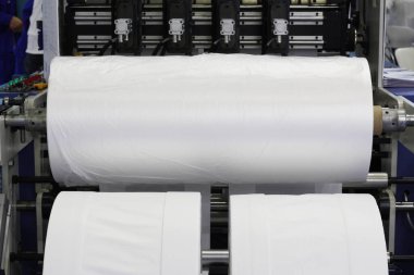 Plastik poşet üretimi için kullanılan bir makine parçası. Fabrikadaki plastik poşet üretimi. Şaftlar dönüyor. Selofan şaftlar arasında hareket eder.
