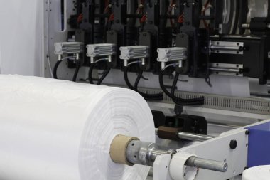 Plastik poşet üretimi için kullanılan bir makine parçası. Fabrikadaki plastik poşet üretimi. Şaftlar dönüyor. Selofan şaftlar arasında hareket eder.