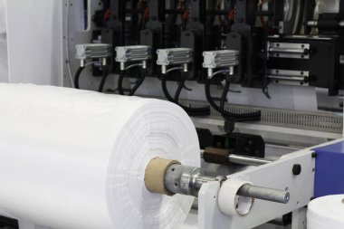 Plastik poşet üretimi için kullanılan bir makine parçası. Fabrikadaki plastik poşet üretimi. Şaftlar dönüyor. Selofan şaftlar arasında hareket eder.