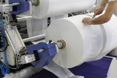 Fabrikadaki usta üretimi takip ediyor. Plastik poşet üretimi için kullanılan bir makine parçası. Fotoğrafta üretim makinesinin ayarlayıcısının elini görebilirsiniz..