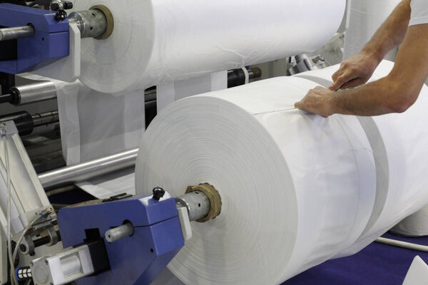 The master at the factory monitors production. A fragment of a machine for the production of plastic bags. In the photo you can see the hand of the adjuster of the production machine.
