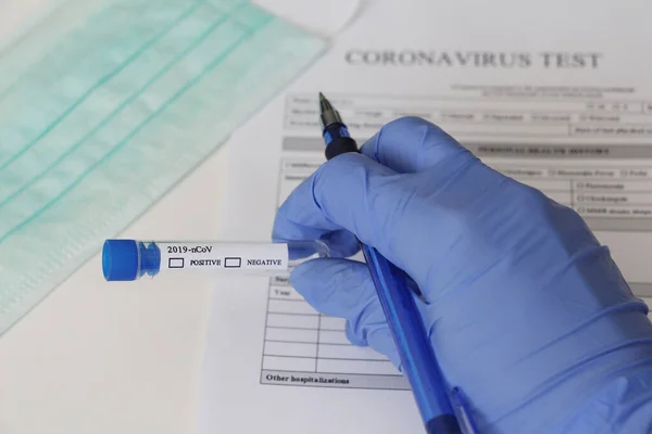 Laboratory test for determination of Coronavirus. Concept. The doctor holds a test tube for analysis. The test tube says POSITIVE and NEGATIVE. On the table lies consent to take the tests.