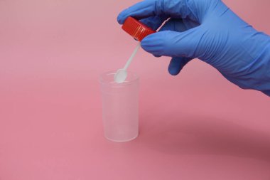 Mavi lateks eldivenli bir el dışkı toplamak için bir kap tutar. Doktorun elinde analiz için plastik kap var. Analiz kavanozu boş. Pembe arkaplan.