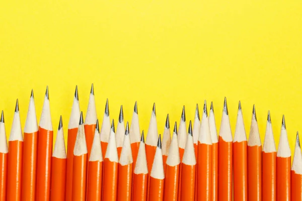 Black lead pencils on a yellow background. Lead pencils. A lot of the same pointed pencils.