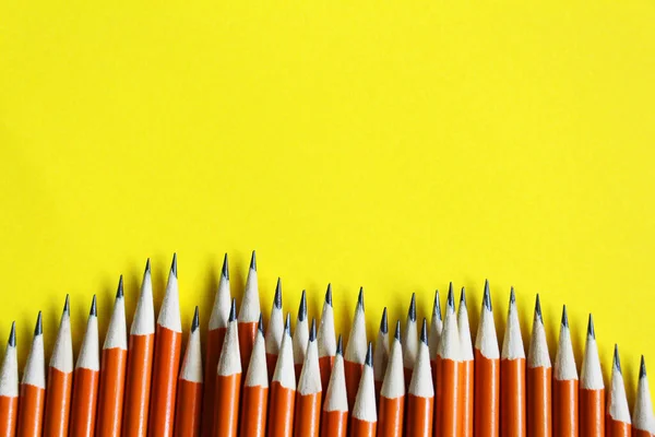 Black lead pencils on a yellow background. Lead pencils. A lot of the same pointed pencils.