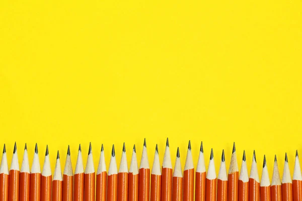 Black lead pencils on a yellow background. Lead pencils. A lot of the same pointed pencils.