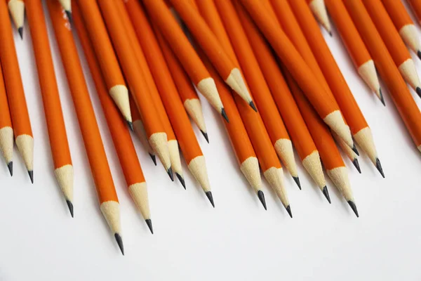 Many black lead pencils on a white background. Lead pencils. A lot of the same pointed pencils.