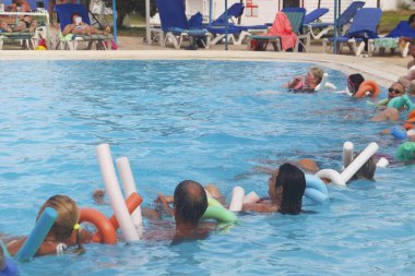 Tunus 06.20.2019. Birkaç kişi havuzda aerobik yapıyor. Tatil yapan turistler. Su aktiviteleri. Havuzdaki mutlu bir grup yüzen eriştelerle su sporu yapıyor..