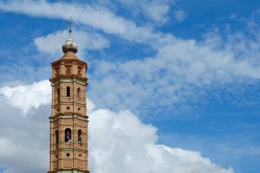 Mudejar tarzı kilise kulesi şehvetli bulutların ve parlak mavi gökyüzünün arkaplanına karşı
