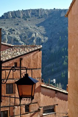 Dar bir kırsal sokakta açık kahverengi bir evin köşesine cam ve metalden yapılmış sokak lambası. Albarakin köyü, Teruel, Aragon, İspanya