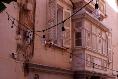 Konforlu bej evlerin arasında, aydınlatma lambaları asılı. Bayram süsü olarak. Valletta 'nın güzel caddesi dar, Malta