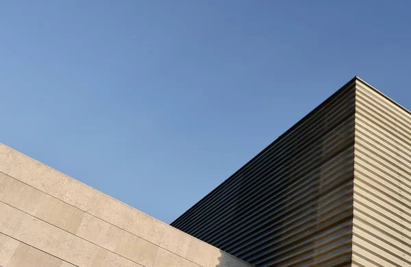 Kenar mahallelerdeki güneş alan geniş ve minimal binanın üçgen köşesi. Asgari şehir detayları, gökyüzüne karşı basit geometrik çizgiler.